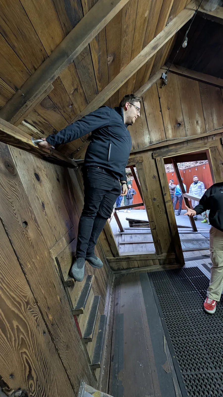 Mark standing at an impossible angle in a tilted wooden house